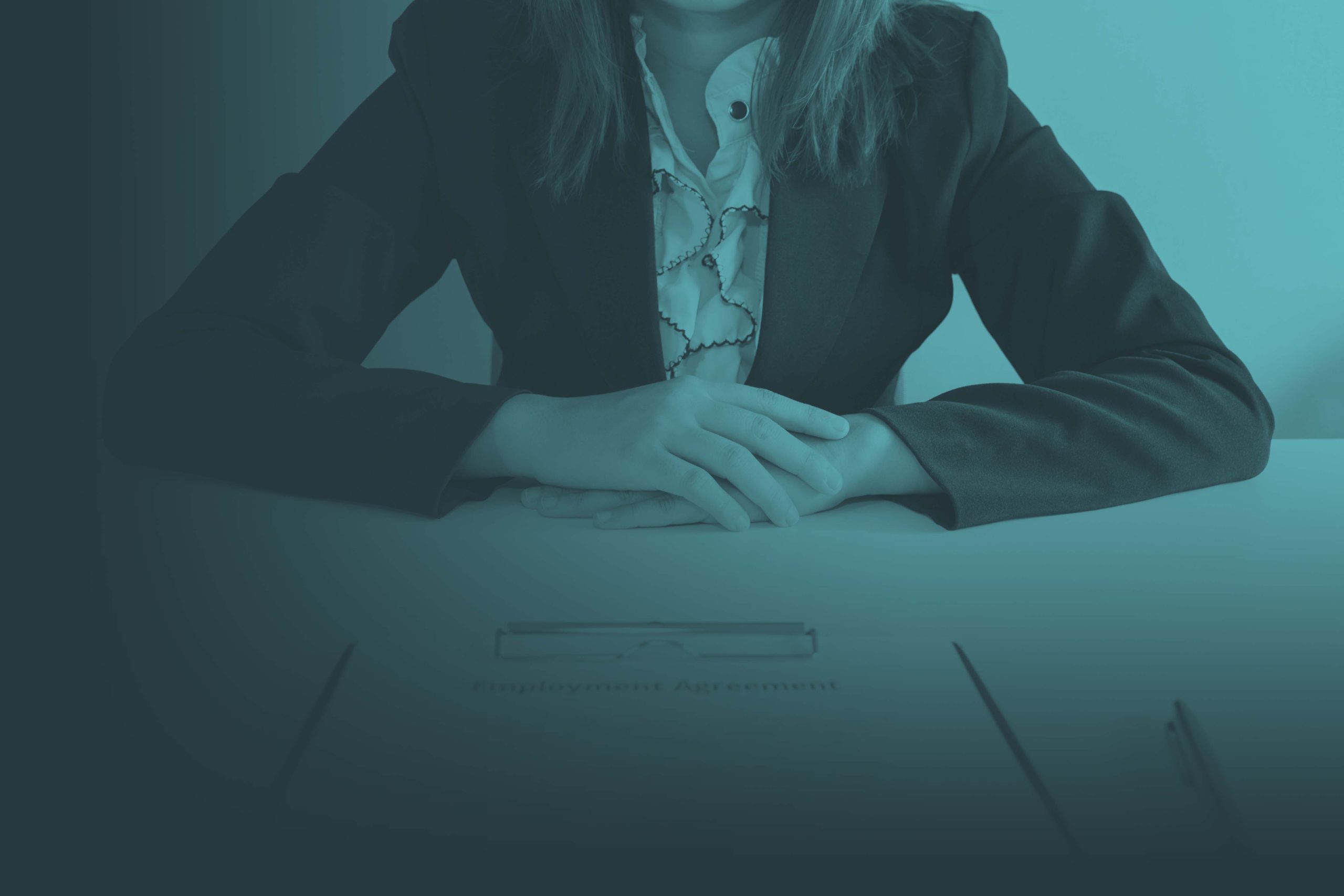 Woman in suit across the desk from paperwork on a clipboard