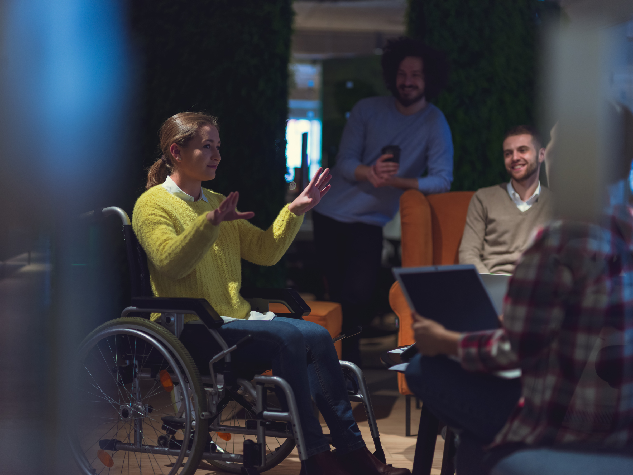 Woman seated in wheelchair addresses colleagues during a workplace discussion.