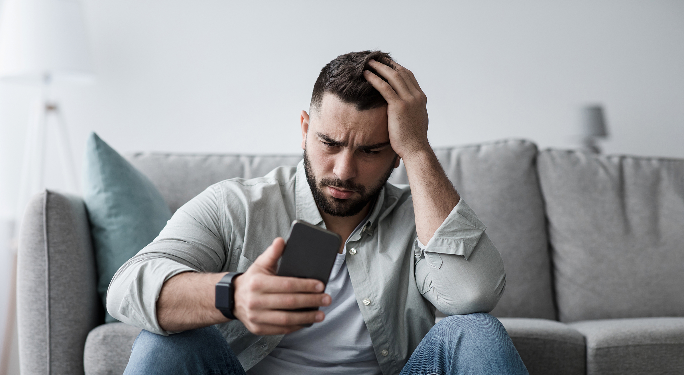 A dejected man looks at his phone after being informed he was fired from his job for his social media posts.